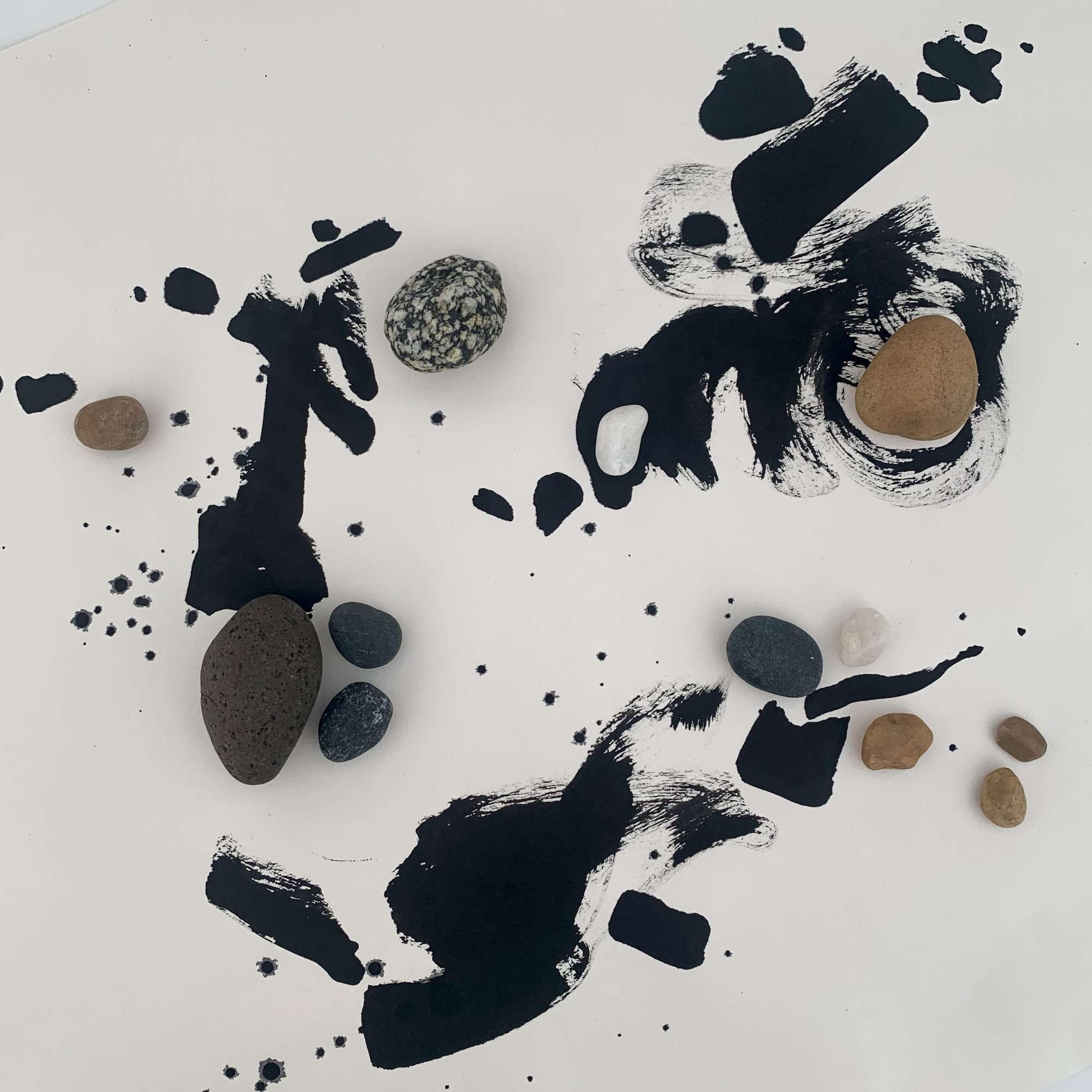 An artwork on pale paper formed by areas of fluid, expressive brushed black ink lines, supplemented by strategically placed rounded pebbles of different sizes, textures and colours, to balance the composition and lead the eye around he space. Three areas of detail, each distinct in the space, all interact with each other.