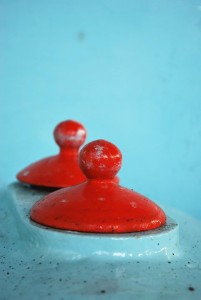 A graphic detail photo of bright red painted round metal caps against aqua green painted metal.
