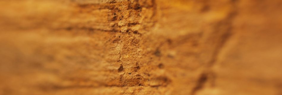 A detail photo of scored marks on the worked face of a block of yellow sandstone. The shot has shallow depth of field, focusing only on the marks.