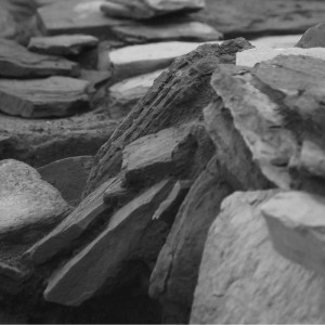 A black and white abstracted photo showing rock slabs sitting at different angles, forming graceful patterns on an archaeological dig site.