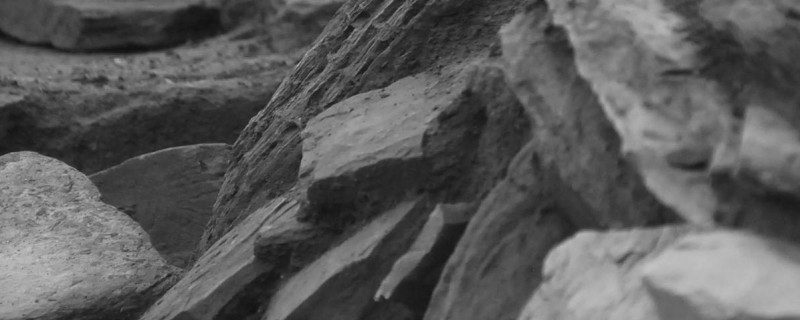 A black and white abstracted photo showing rock slabs sitting at different angles, forming graceful patterns on an archaeological dig site.