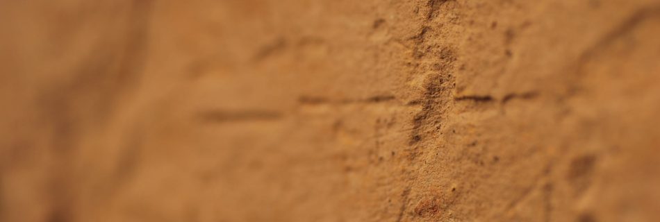 A detail photo of scored marks on the worked face of a block of yellow sandstone. The shot has shallow depth of field, focusing only on the marks.