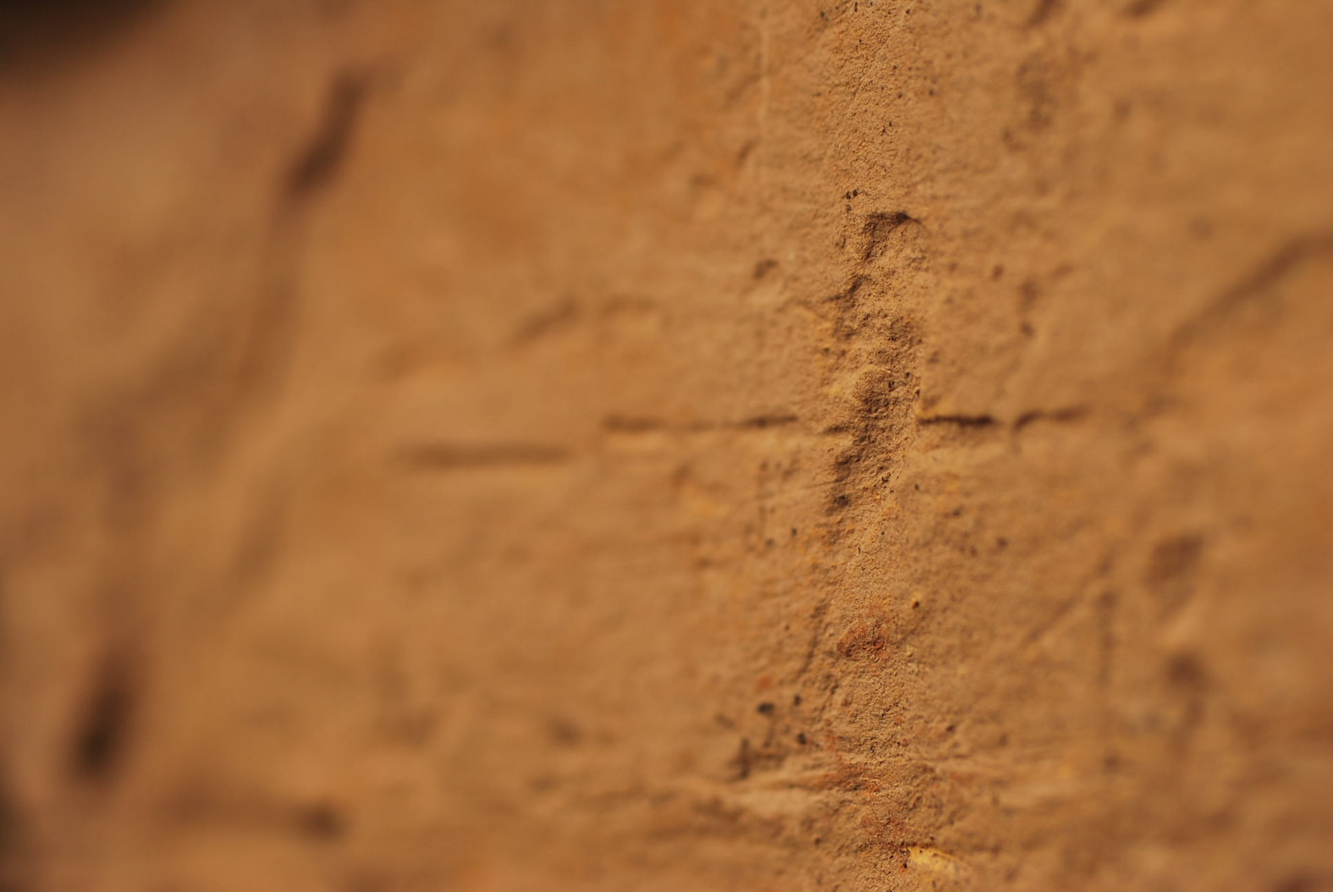 A detail photo of scored marks on the worked face of a block of yellow sandstone. The shot has shallow depth of field, focusing only on the marks.
