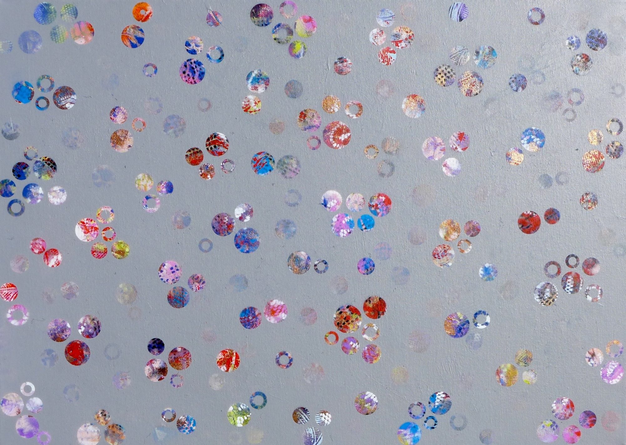 A landscape orientation canvas with mid grey ground. On it are arranged randomly many small dots and rings, each filled with textural pattern, in vivid colours - blues, reds, pinks, purples, with some whites and yellows.