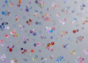 A landscape orientation canvas with mid grey ground. On it are arranged randomly many small dots and rings, each filled with textural pattern, in vivid colours - blues, reds, pinks, purples, with some whites and yellows.
