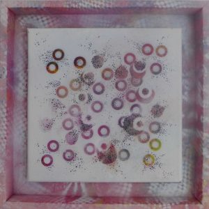 a small square canvas with an arrangement of dots and ring shapes in soft reds, pinks and purples, agmented by tiny black pin dots. Sits within a wooden tray frame that's painted with abstract pattern and colour to match the dots.