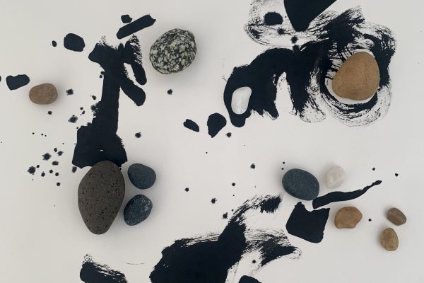 An artwork on pale paper formed by areas of fluid, expressive brushed black ink lines, supplemented by strategically placed rounded pebbles of different sizes, textures and colours, to balance the composition and lead the eye around he space. Three areas of detail, each distinct in the space, all interact with each other.