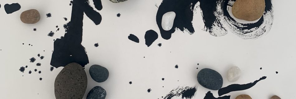 An artwork on pale paper formed by areas of fluid, expressive brushed black ink lines, supplemented by strategically placed rounded pebbles of different sizes, textures and colours, to balance the composition and lead the eye around he space. Three areas of detail, each distinct in the space, all interact with each other.